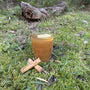 A hot toddy made with black tea and spiced rum sitting on a grass flat with a log in the background.